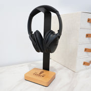 Personalised headphone stand engraved with a name, featuring a beech wood base and black aluminium holder.
