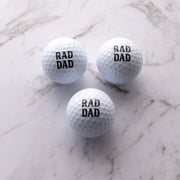 Three premium golf balls printed with "Rad Dad" and presented in a black gift box for golf-loving dads.