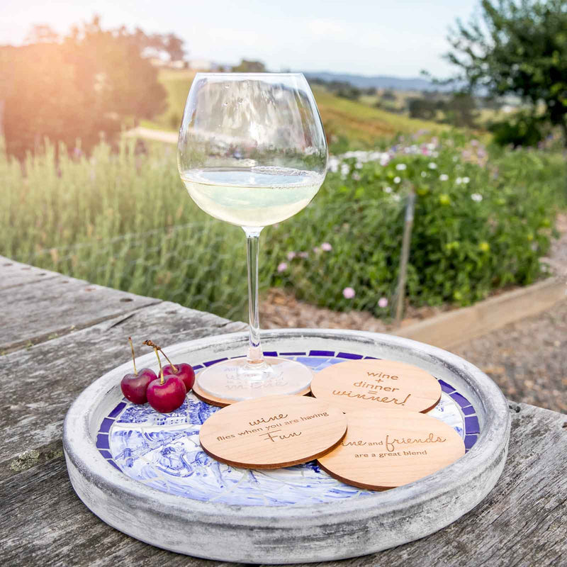 Wine glass resting on engraved wooden coaster with humorous wine wisdom